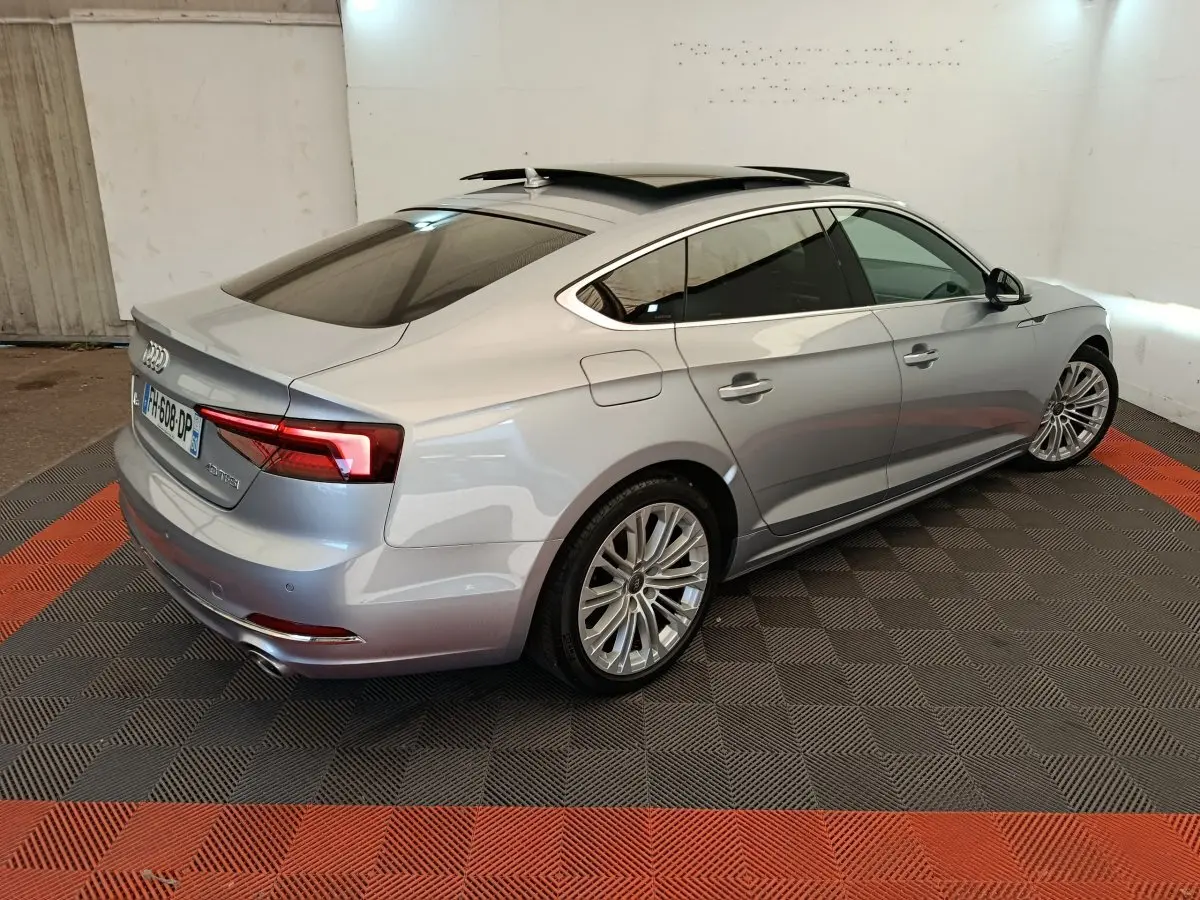 Audi A5 gris clair vue 3/4 arrière droit, toit ouvrant et feux arrière LED dans un garage intérieur.