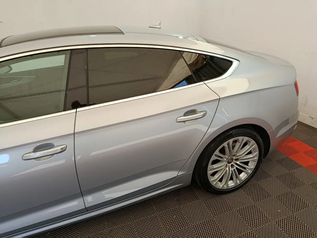 Vue côté droit arrière d'une Audi A5 gris clair avec jante alliage et vitres teintées dans un intérieur fermé.