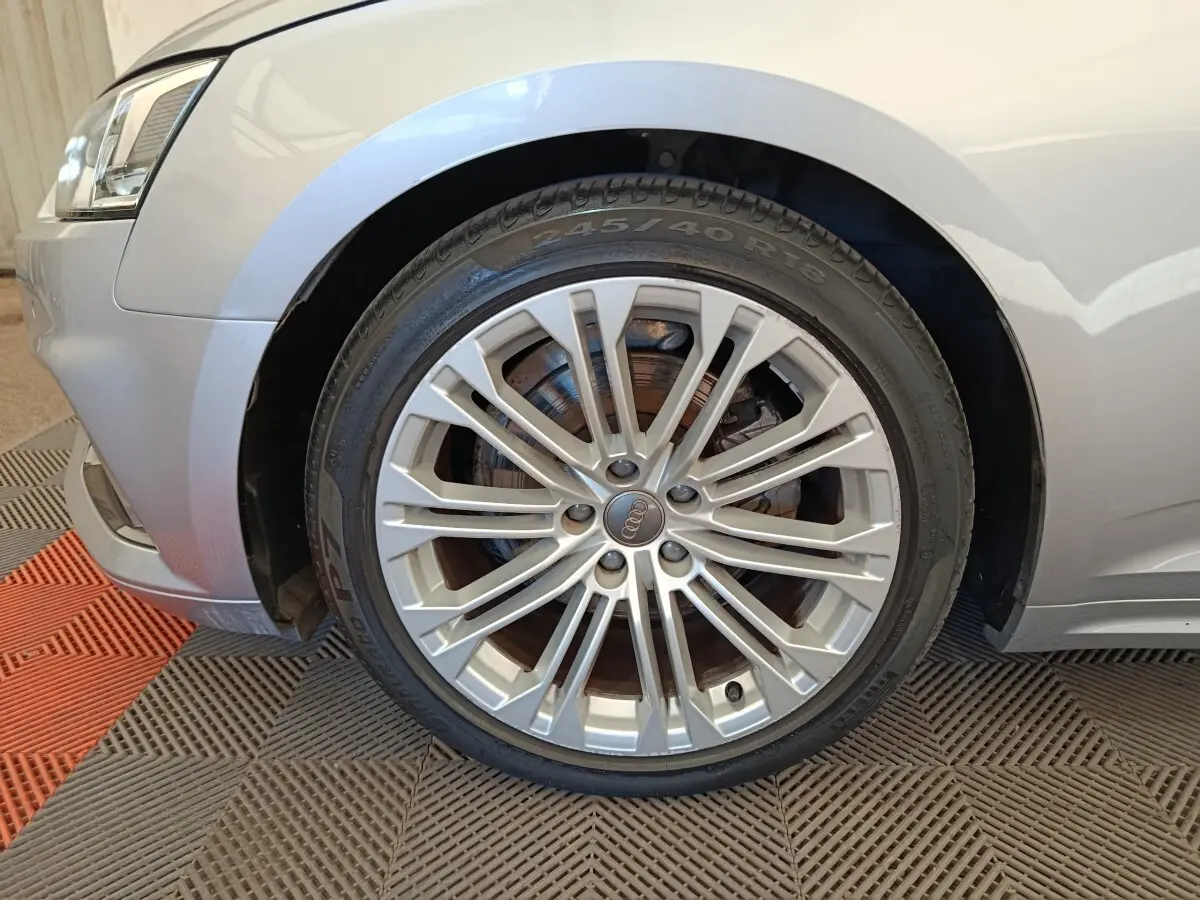 Gros plan sur la roue avant gauche et l'aile gris clair d'une Audi A5 40 TFSI 2019 avec jante alliage multibranches.