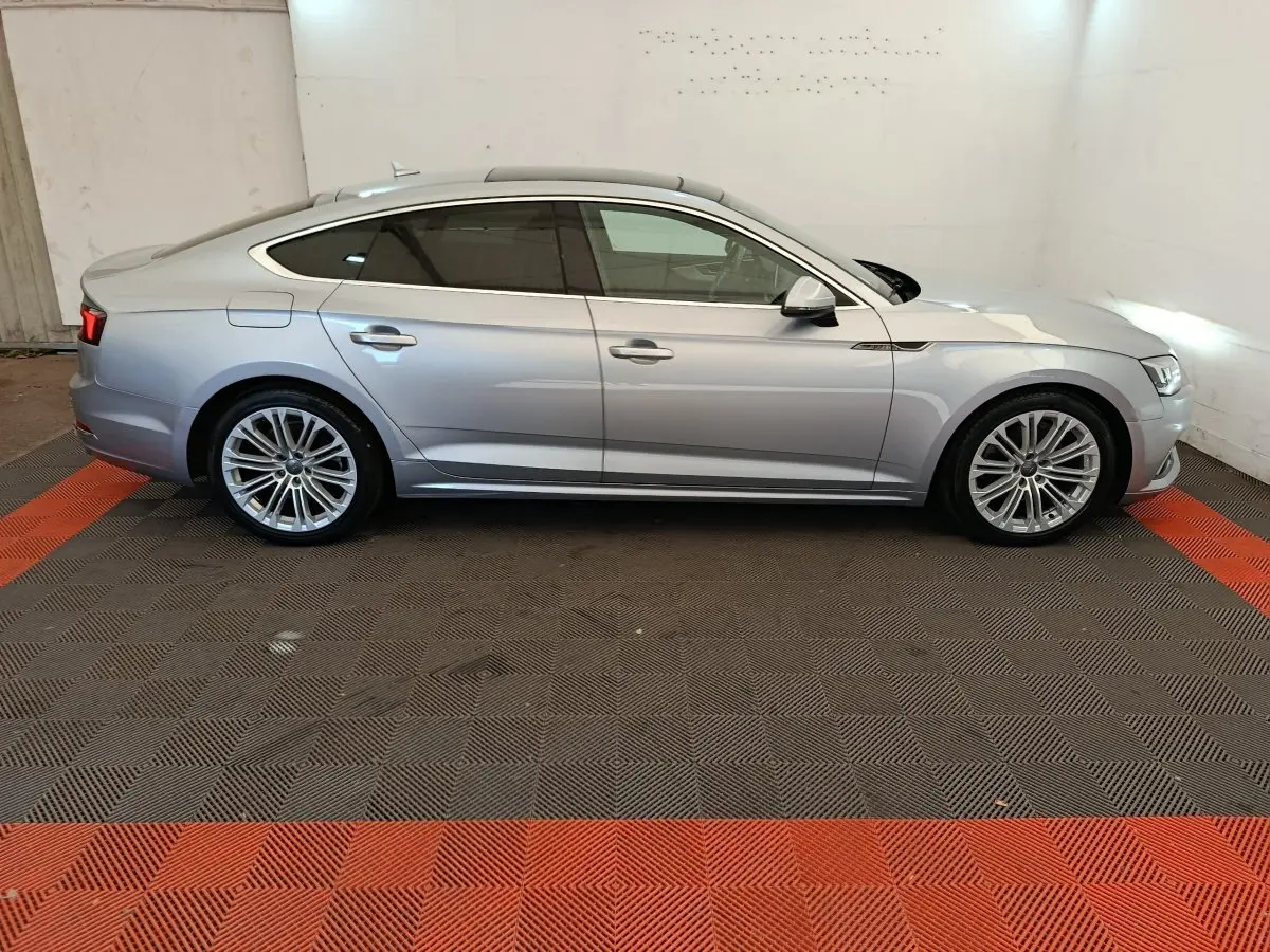 Profil côté gauche d'une Audi A5 gris clair 2019 avec jantes alliage et toit panoramique visible en intérieur.