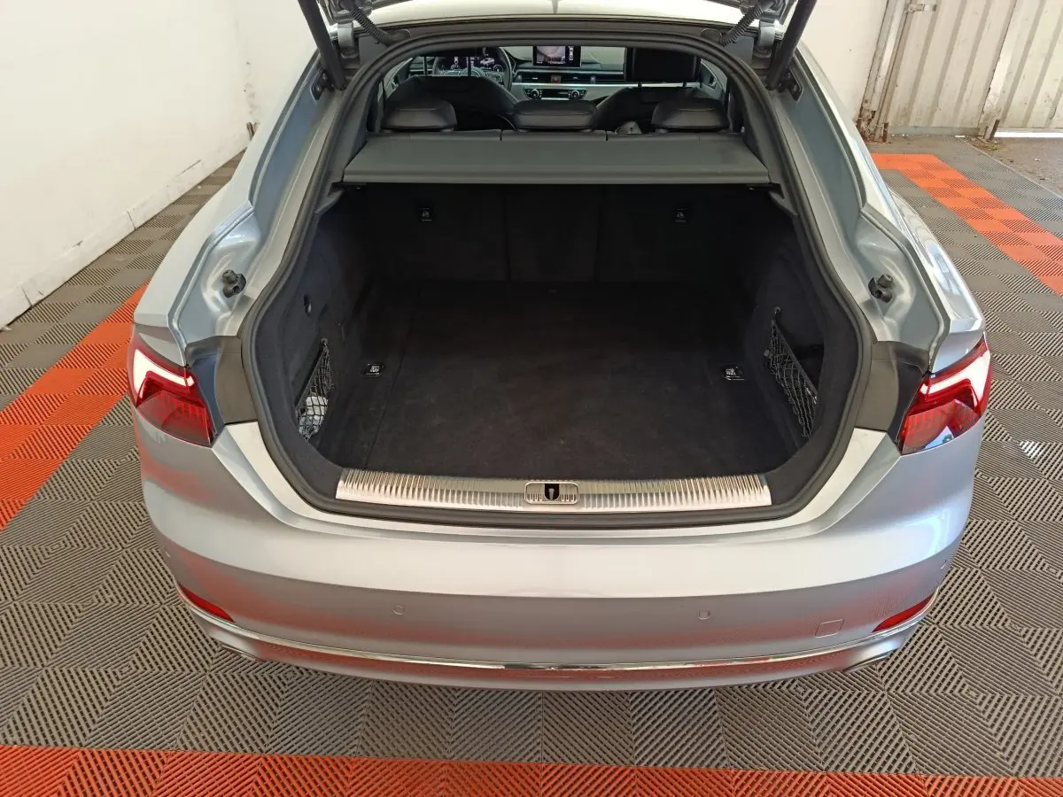 Coffre ouvert vu de l'arrière d'une Audi A5 gris clair, montrant un espace de chargement spacieux et propre.