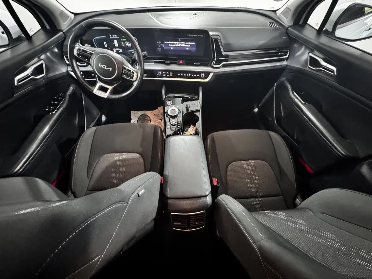 Vue intérieure avant du Kia Sportage blanc 2024, tableau de bord moderne avec écran tactile et volant multifonctions cuir.