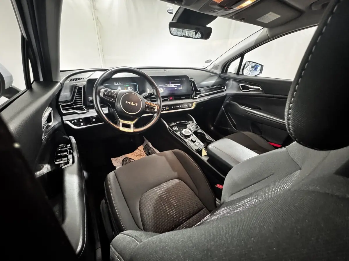 Vue intérieure avant droite du Kia Sportage 2024, tableau de bord noir avec écran tactile et volant cuir multifonctions.