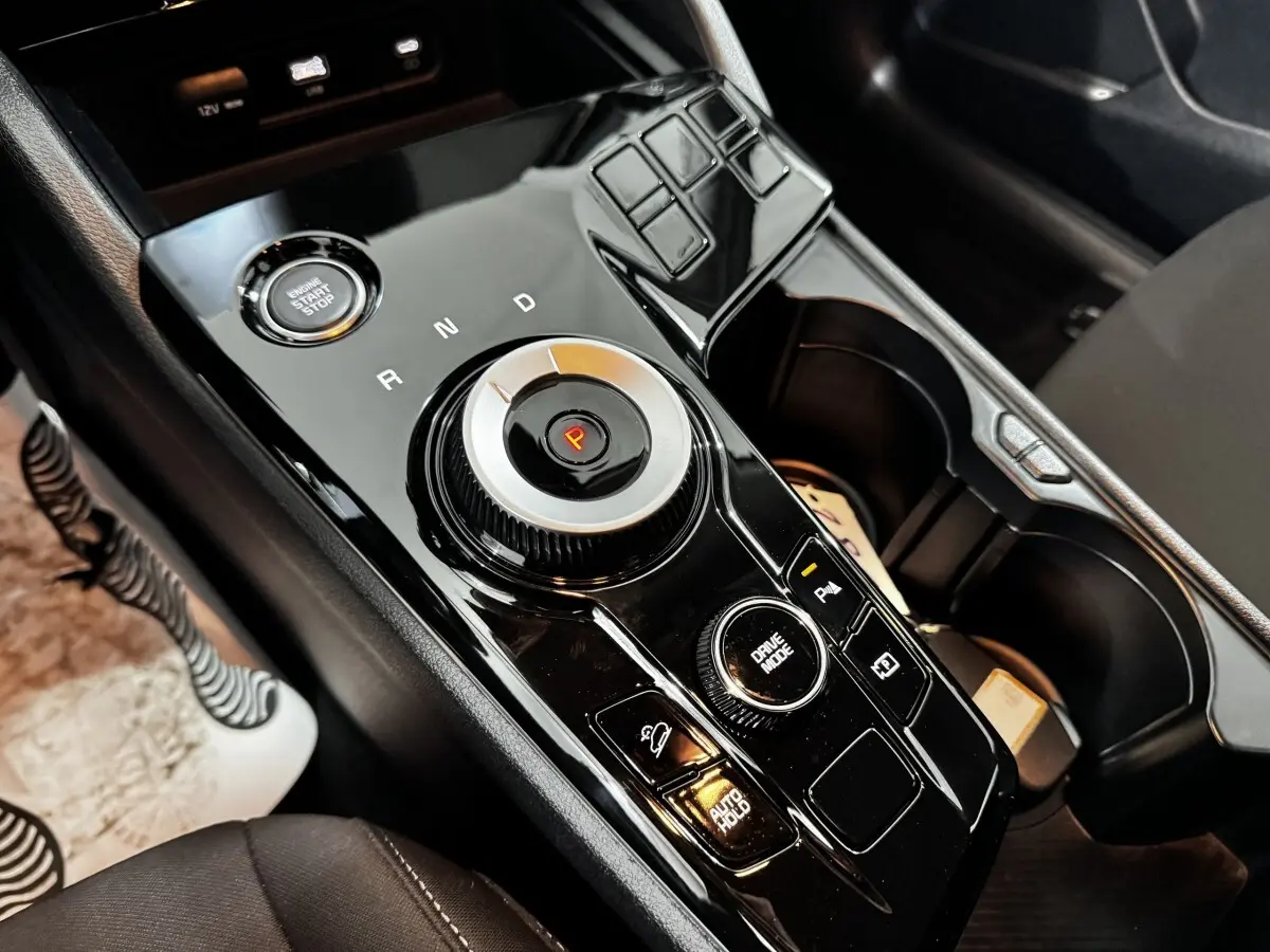 Gros plan sur la console centrale noire brillante du Kia Sportage 2024, avec molette de sélection de vitesse et bouton start/stop.