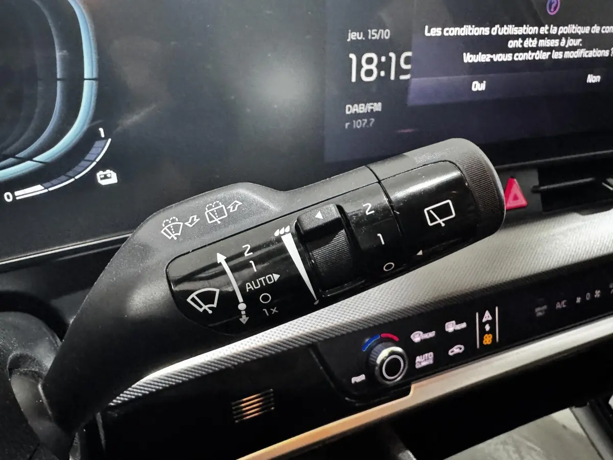 Gros plan sur la commande des essuie-glaces du tableau de bord numérique du Kia Sportage blanc 2024, affichage multifonctions visible.