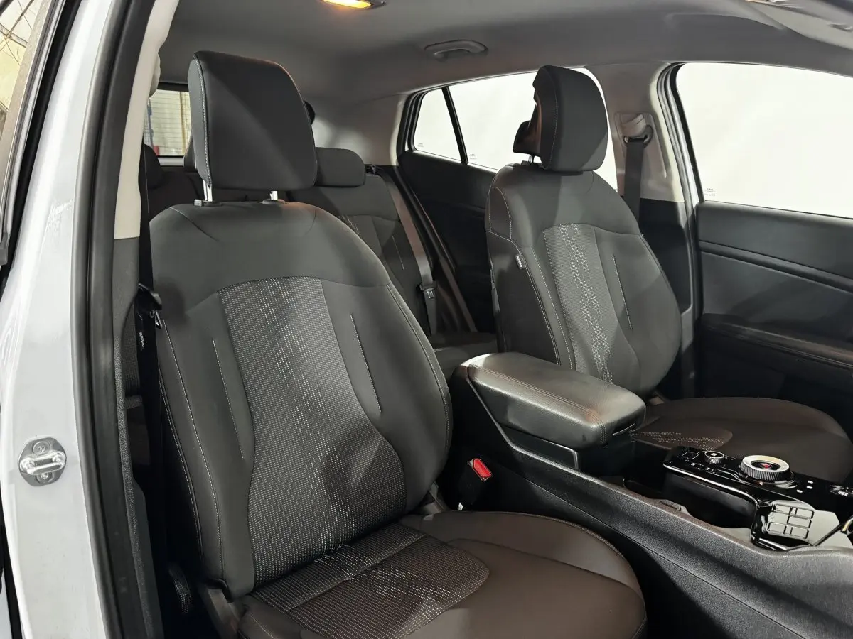 Vue intérieure côté gauche du Kia Sportage 2024 blanc, mettant en valeur les sièges avant noirs et la console centrale.