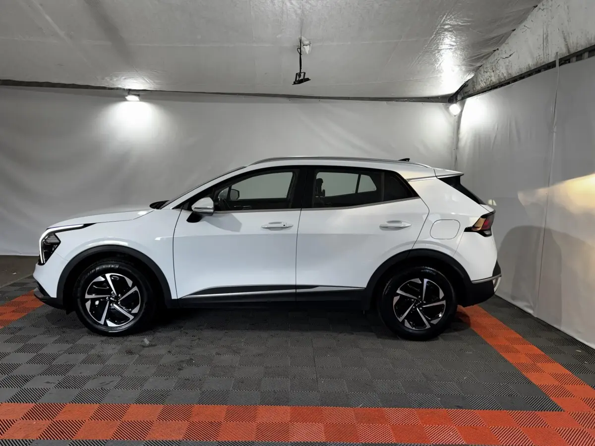 Vue de profil côté gauche d’un KIA Sportage blanc 2024 avec jantes noires et détails noirs sur les bas de caisse.