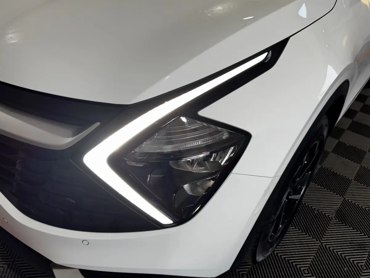 Gros plan sur le phare avant droit blanc du Kia Sportage 2024 avec signature lumineuse LED en forme de flèche.