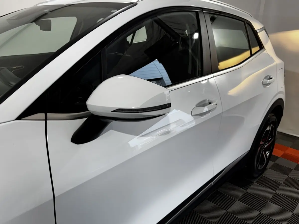 Vue côté gauche du Kia Sportage blanc 2024, mettant en valeur la porte arrière et le rétroviseur avec clignotant intégré.