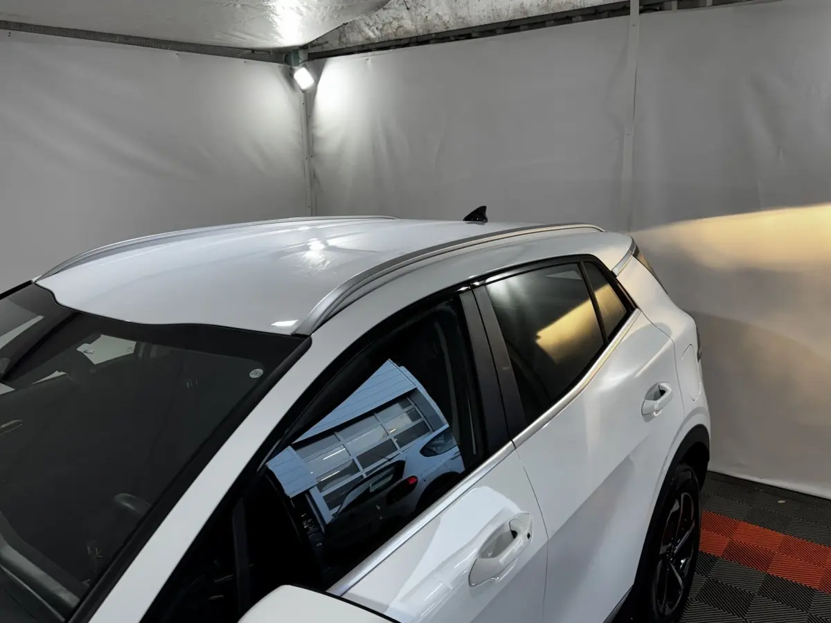 Vue 3/4 arrière droite du KIA SPORTAGE blanc 2024 avec toit et vitres teintées dans un garage fermé.