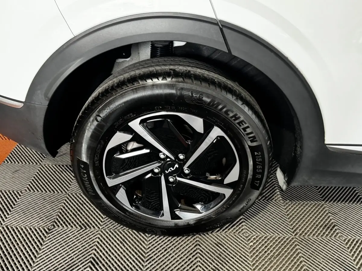 Gros plan sur la roue arrière droite d’un KIA Sportage blanc 2024 avec jante alliage noire et argentée.