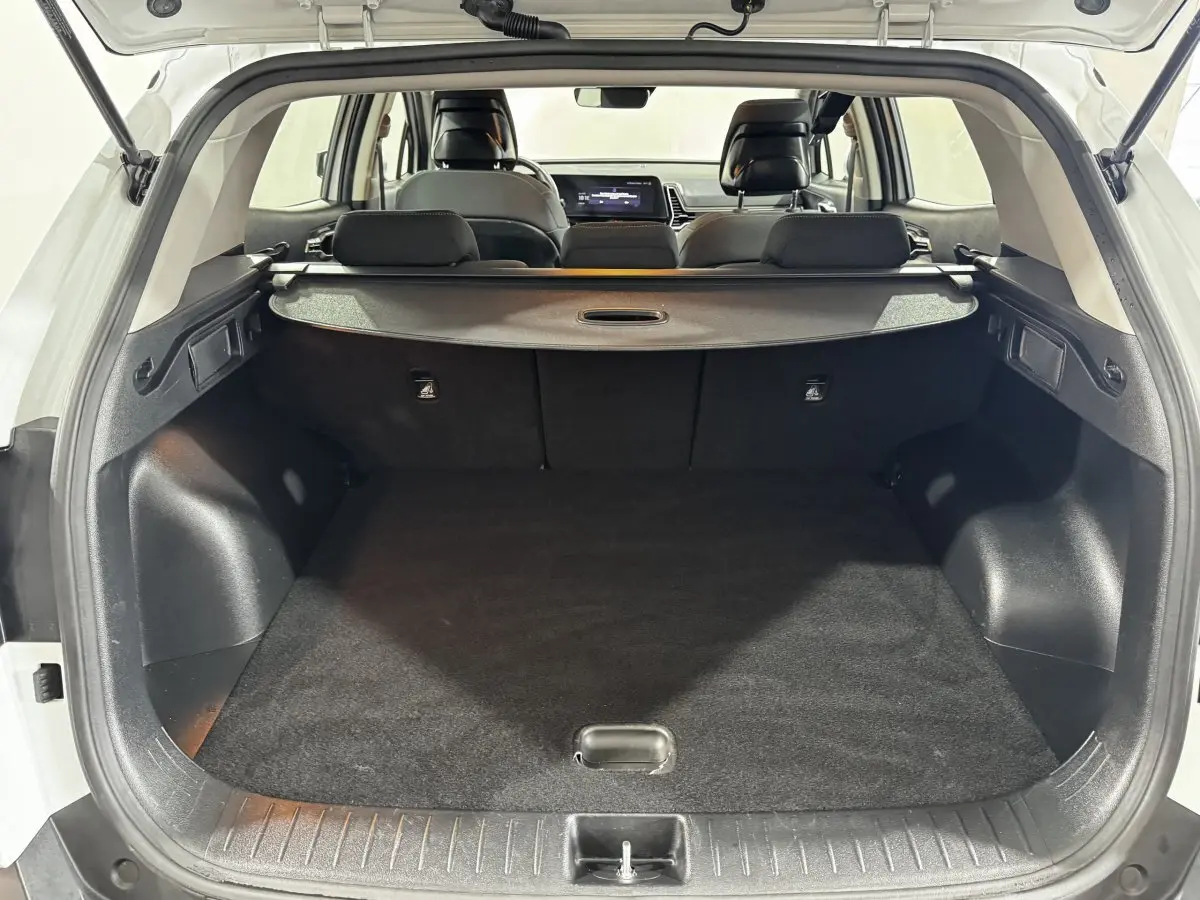 Coffre ouvert d’un KIA Sportage blanc 2024, vue arrière montrant l’espace de chargement et la tablette cache-bagages.