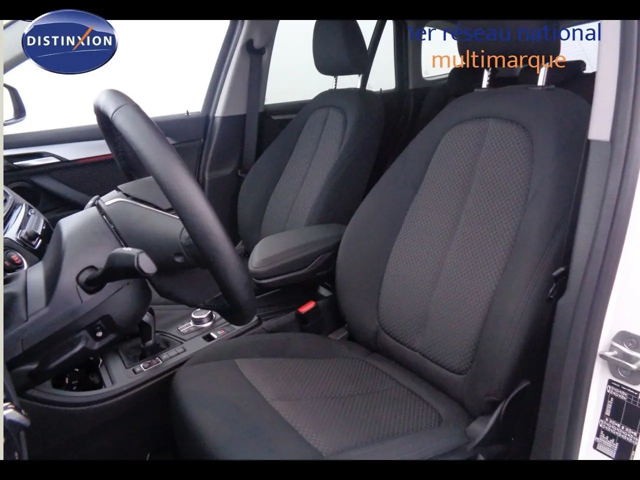 Intérieur du BMW X1 blanc Alpine, vue côté conducteur sur les sièges noirs en tissu et le tableau de bord moderne.