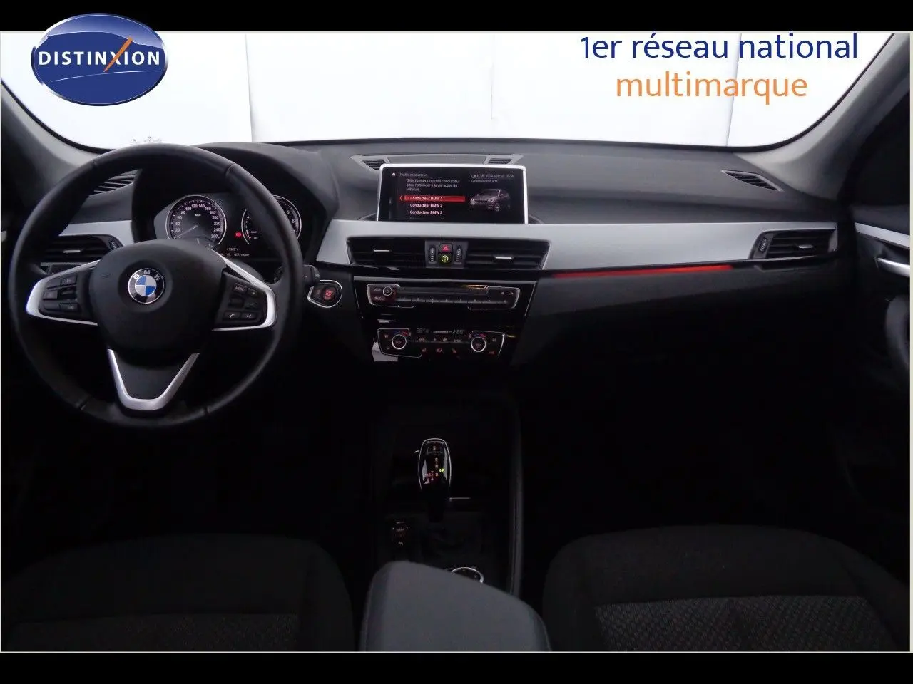 Intérieur avant d'une BMW X1 blanc Alpine, tableau de bord moderne avec écran central et volant multifonction noir.