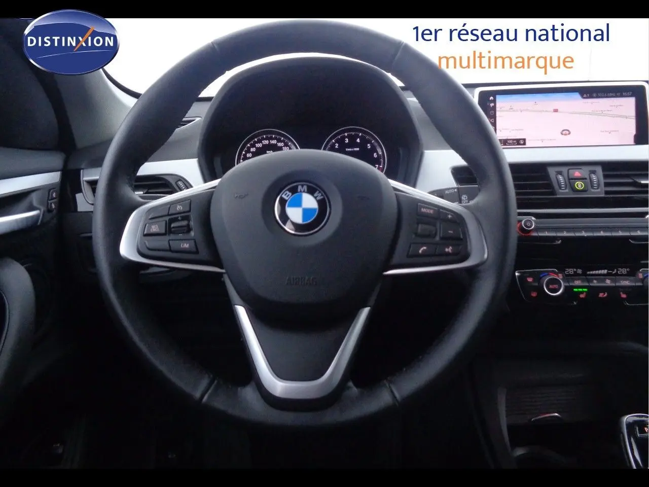 Vue centrée sur le volant BMW d'un X1 blanc Alpine 2022, avec tableau de bord numérique et écran tactile de navigation.