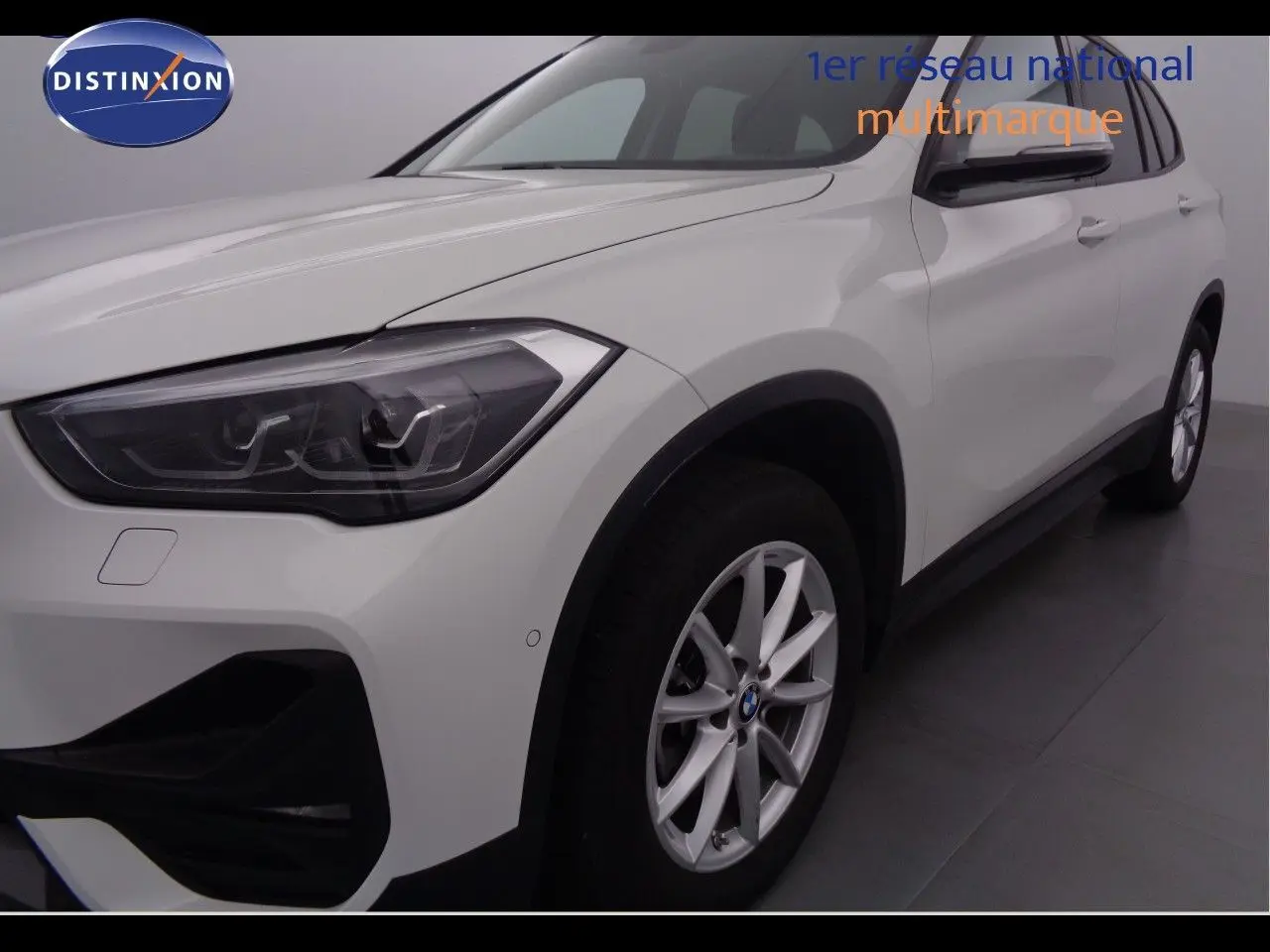 Vue 3/4 avant droit d'un BMW X1 blanc Alpine Metal avec jantes alliage et phares LED distinctifs.