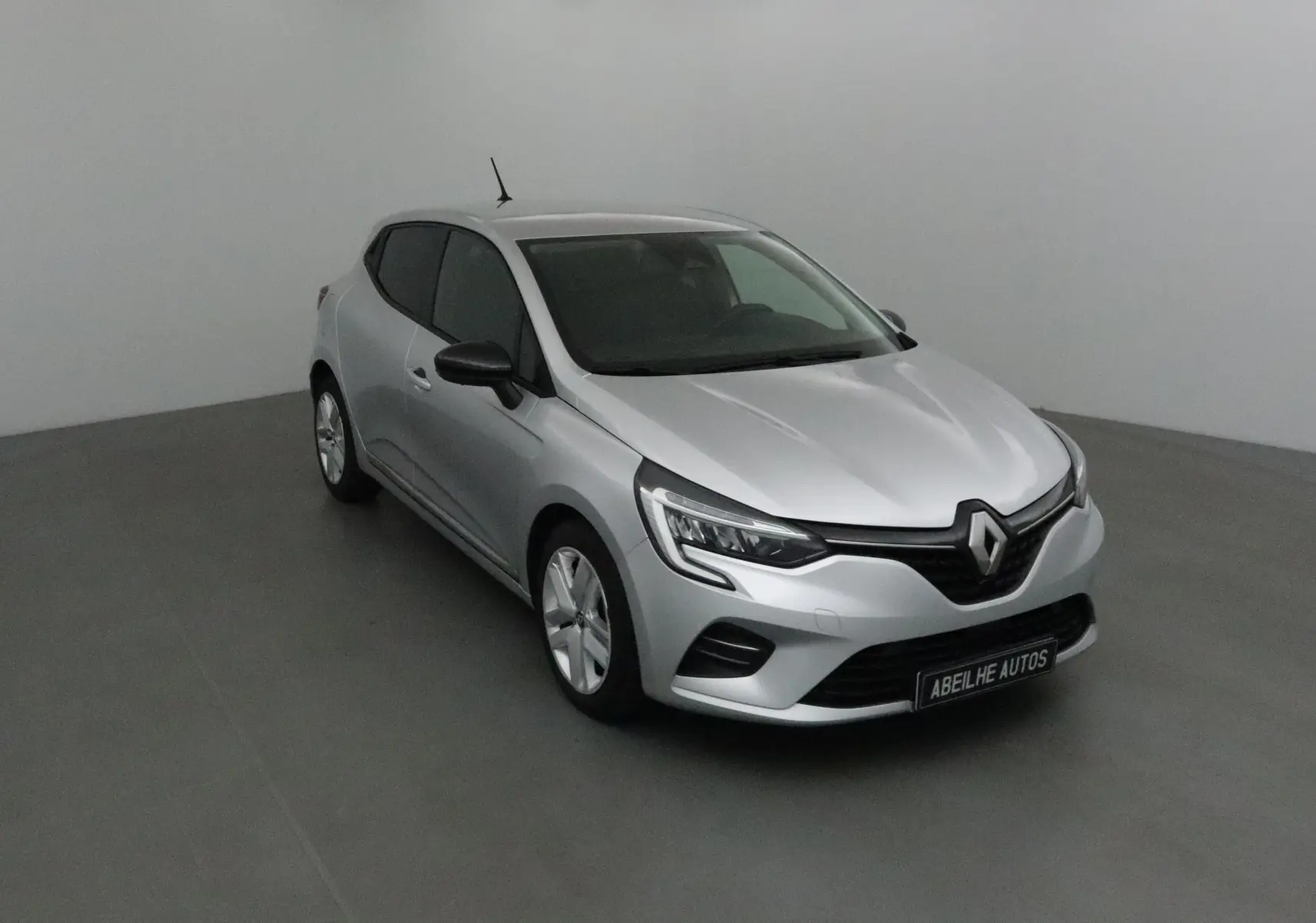 Renault Clio V gris platine vue 3/4 avant droit dans un studio, avec calandre noire et phares LED marqués.
