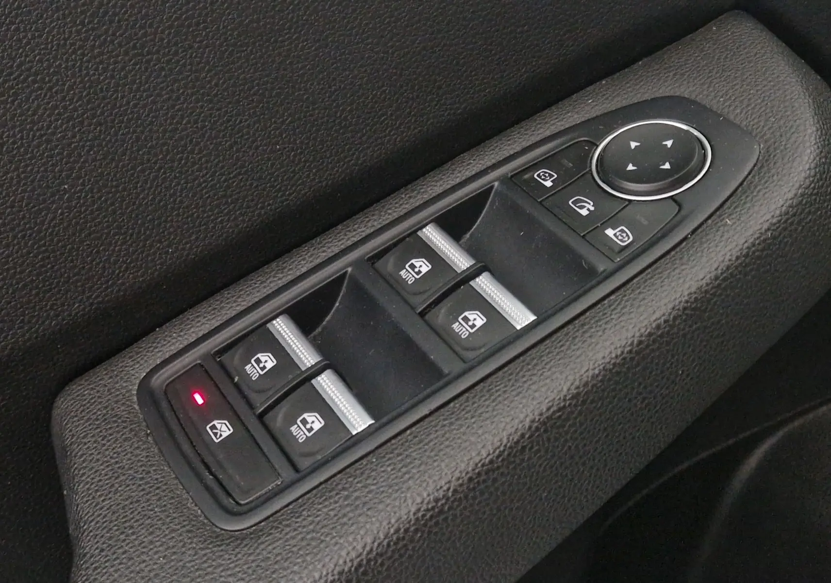 Gros plan sur les commandes électriques des vitres et rétroviseurs côté conducteur de la Renault Clio V gris platine 2021.