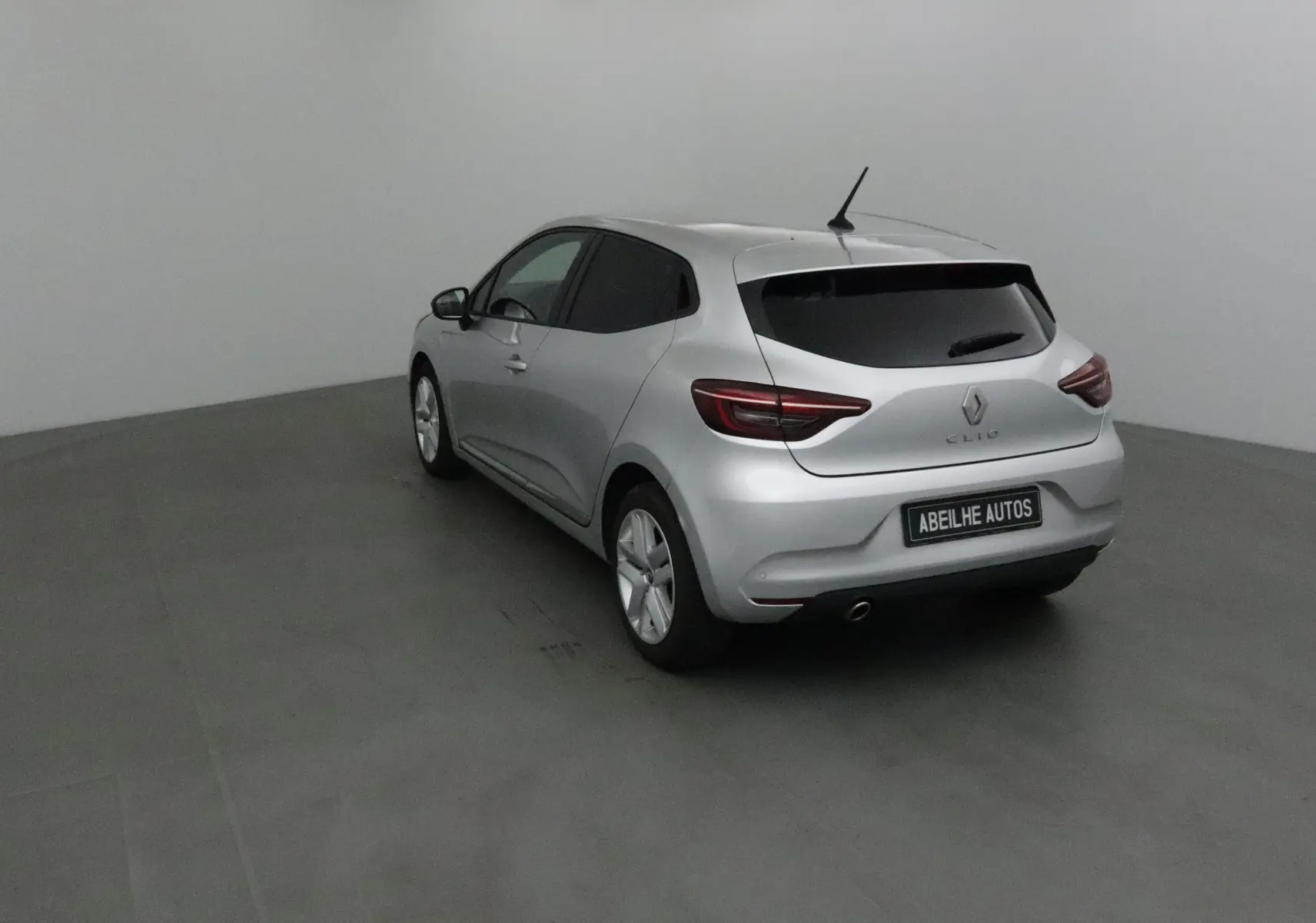 Renault Clio V gris platine vue 3/4 arrière droit dans un studio, avec vitres teintées et feux LED.