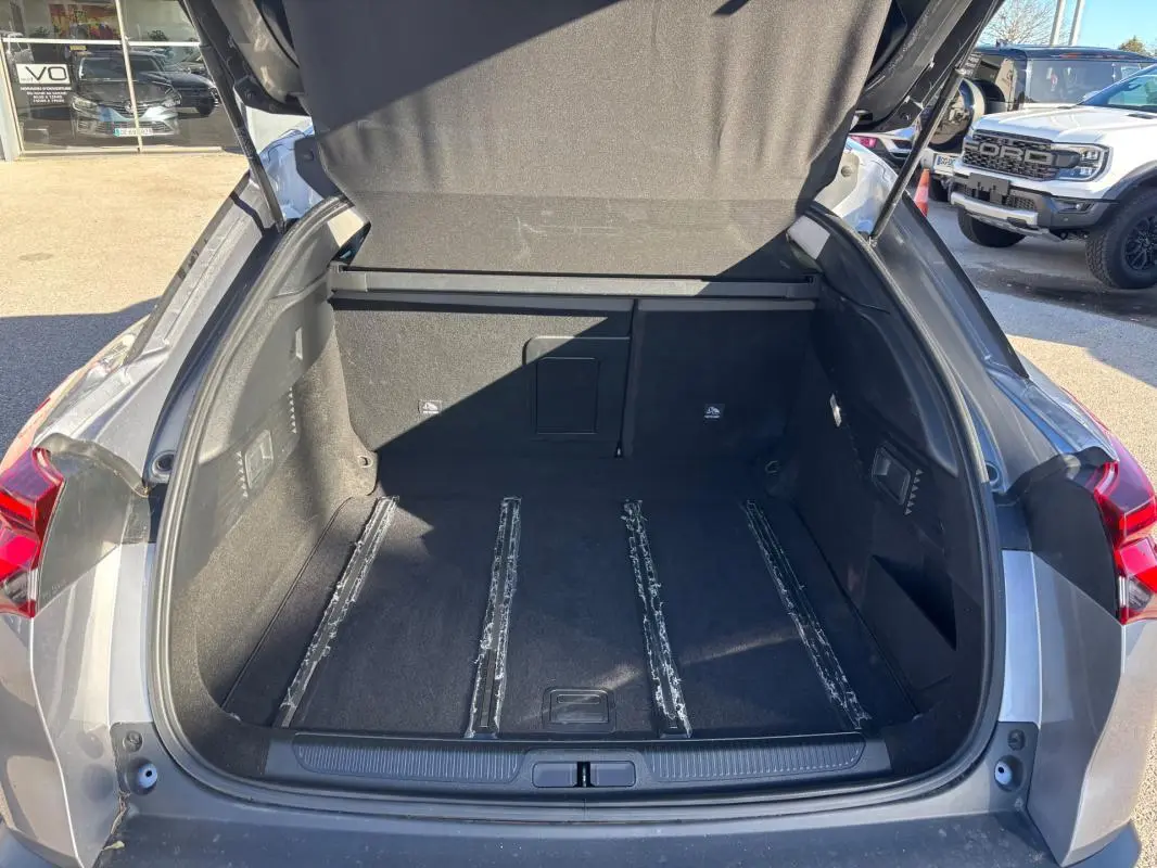 Coffre ouvert vu de l'arrière d'une Citroën C5 X gris foncé, montrant l'espace de chargement vide et les rails au sol.