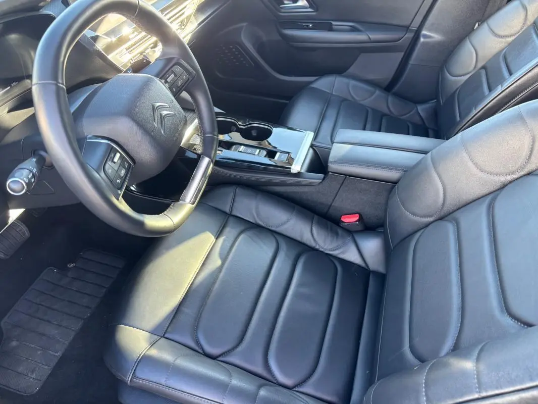 Vue intérieure en plongée du poste de conduite et des sièges en cuir noir du Citroën C5 X 2024 avec accoudoir central et volant cuir.