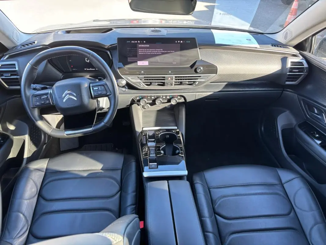 Vue intérieure avant de la Citroën C5 X 2024 avec tableau de bord moderne, écran tactile et sièges cuir noirs.