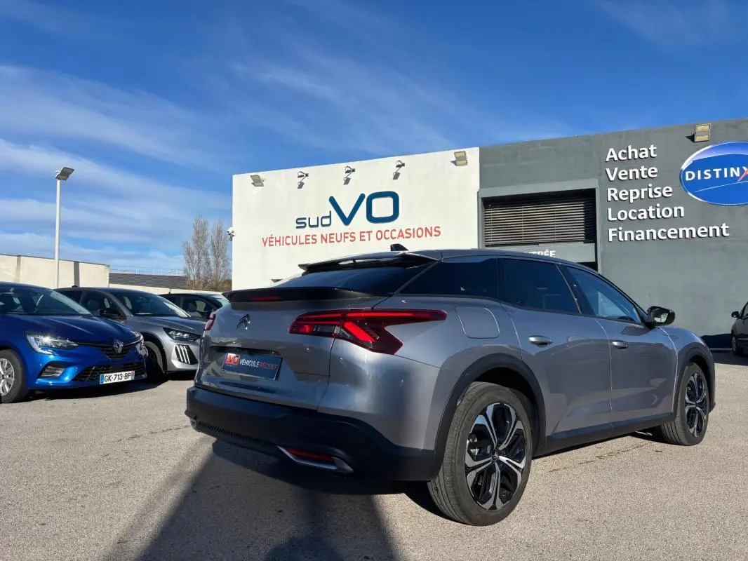 Vue 3/4 arrière droite d'une Citroën C5 X gris foncé avec jantes alliage 19 pouces, barres de toit et vitres teintées.