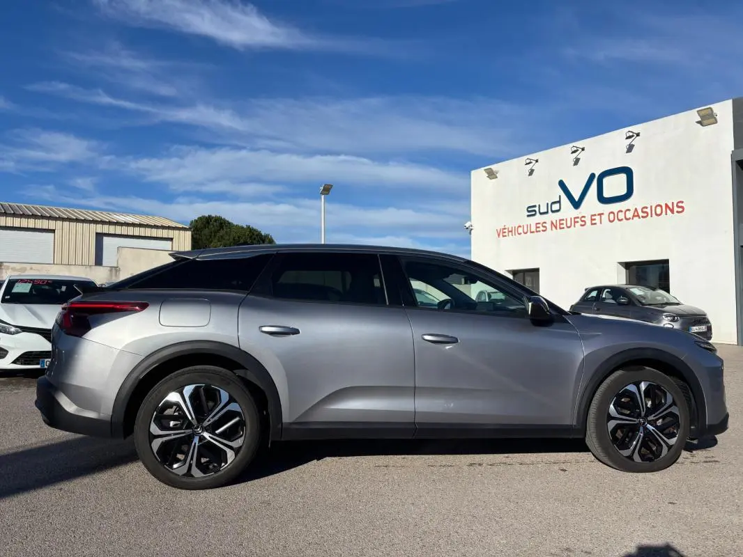 Profil côté gauche du Citroën C5 X gris foncé 2024 avec jantes alliage 19 pouces et barres de toit visibles.