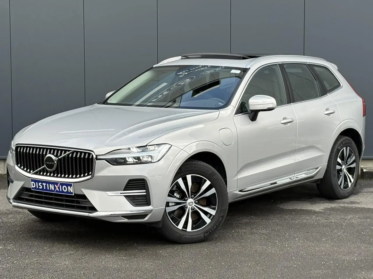 Volvo XC60 T6 AWD gris silver en 3/4 avant droit, avec jantes alliage et toit ouvrant panoramique visible.