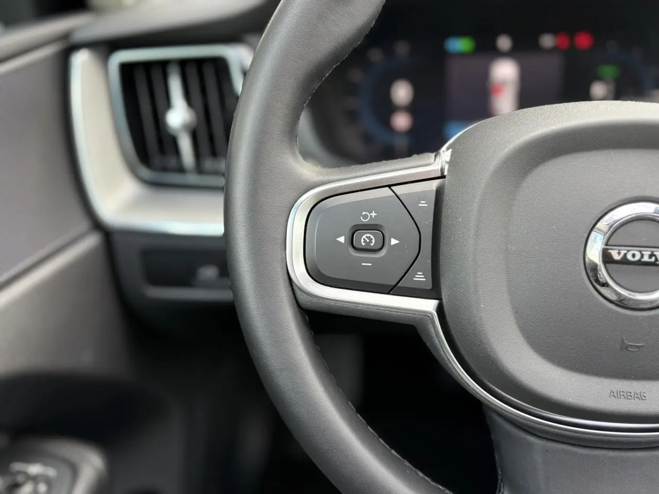 Gros plan sur la partie gauche du volant simili-cuir gris du Volvo XC60 T6 AWD PHEV 2024 avec commandes intégrées.