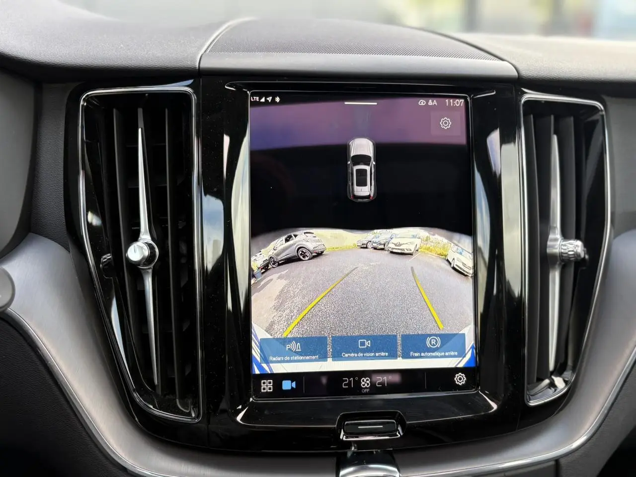 Écran tactile central affichant la caméra de recul du Volvo XC60 gris silver, entouré de deux aérateurs verticaux noirs.