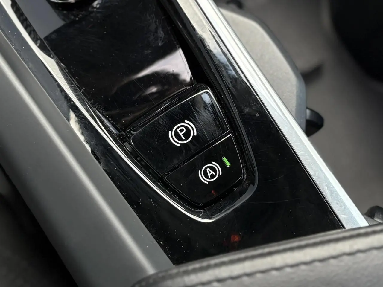 Gros plan sur la console centrale noire brillante du Volvo XC60 2024, montrant les boutons de frein de parking et start/stop.