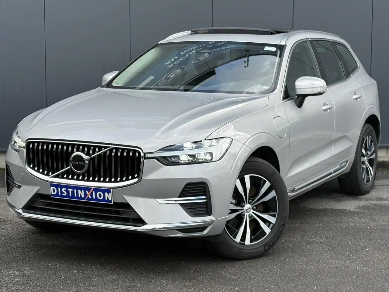 Volvo XC60 T6 AWD PHEV gris silver en 3/4 avant droit, avec calandre chromée et jantes alliage 18 pouces.