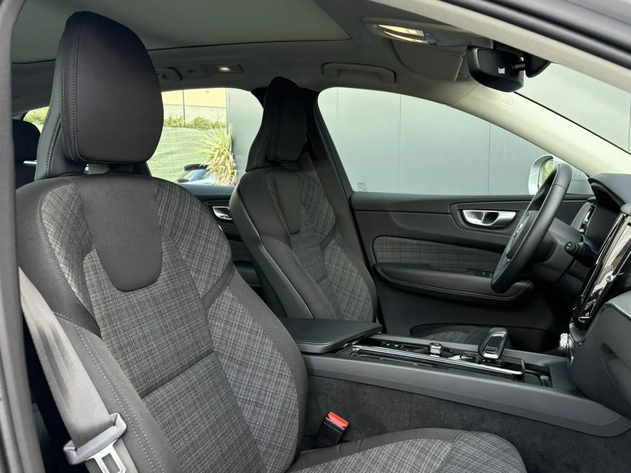 Vue intérieure côté gauche du Volvo XC60 2024, sièges en tissu gris à motif tartan et console centrale noire brillante.