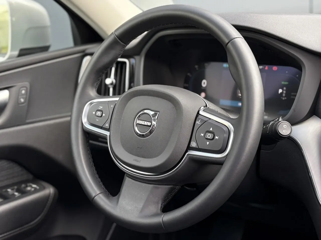 Volant simili-cuir noir de Volvo XC60 2024 vu de face, avec commandes intégrées et tableau de bord digital.