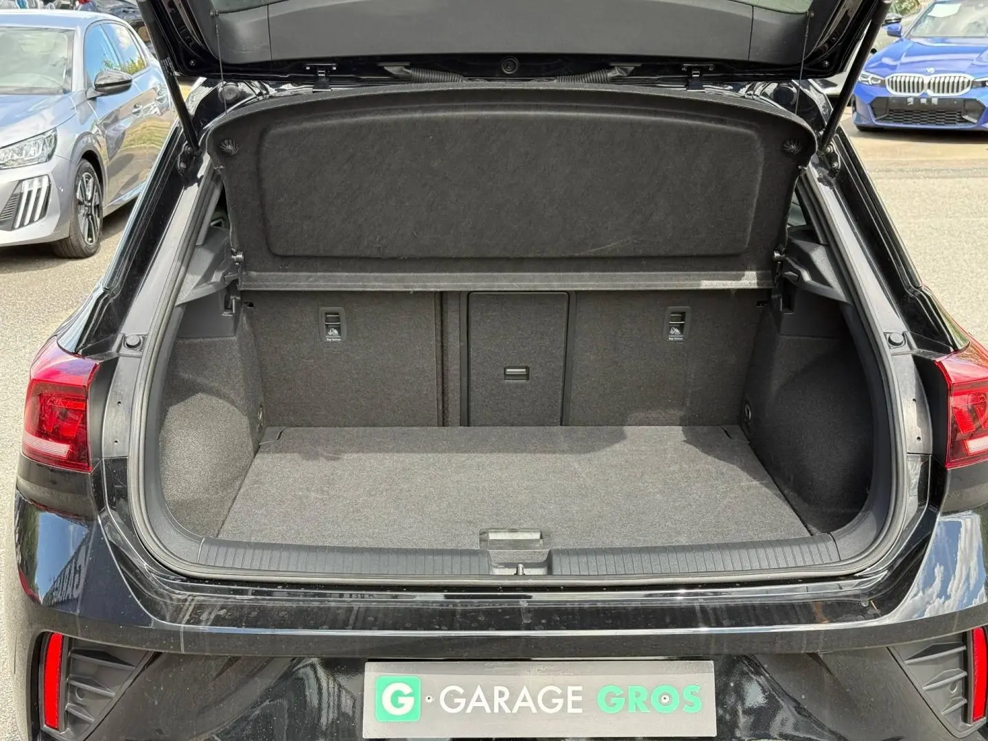 Coffre ouvert vu de l'arrière d'un Volkswagen T-Roc noir intense nacré, avec intérieur de coffre gris et banquette rabattable.