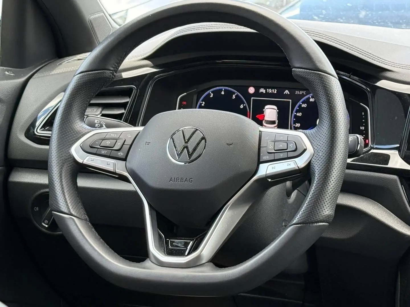 Vue rapprochée du volant cuir multifonction noir du Volkswagen T-Roc 2025 avec tableau de bord numérique en arrière-plan.