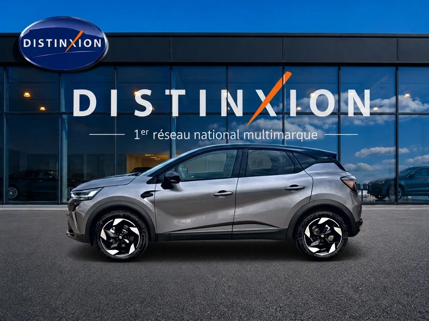 Profil droit d'un Renault Captur 1.8 e-tech hybride 2026 gris Cassiope avec toit noir devant un showroom Distinxion.
