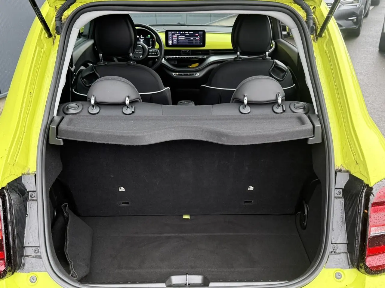 Vue arrière du coffre ouvert d'une FIAT 500 électrique jaune Acid, avec intérieur noir et tableau de bord visible.