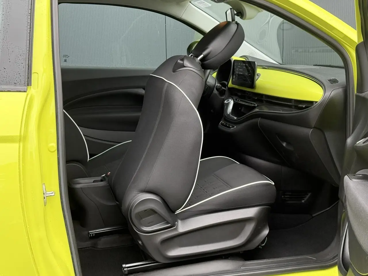 Vue intérieure côté conducteur de la Fiat 500 électrique 2024 avec tableau de bord jaune Acid et sièges noirs à surpiqûres blanches.