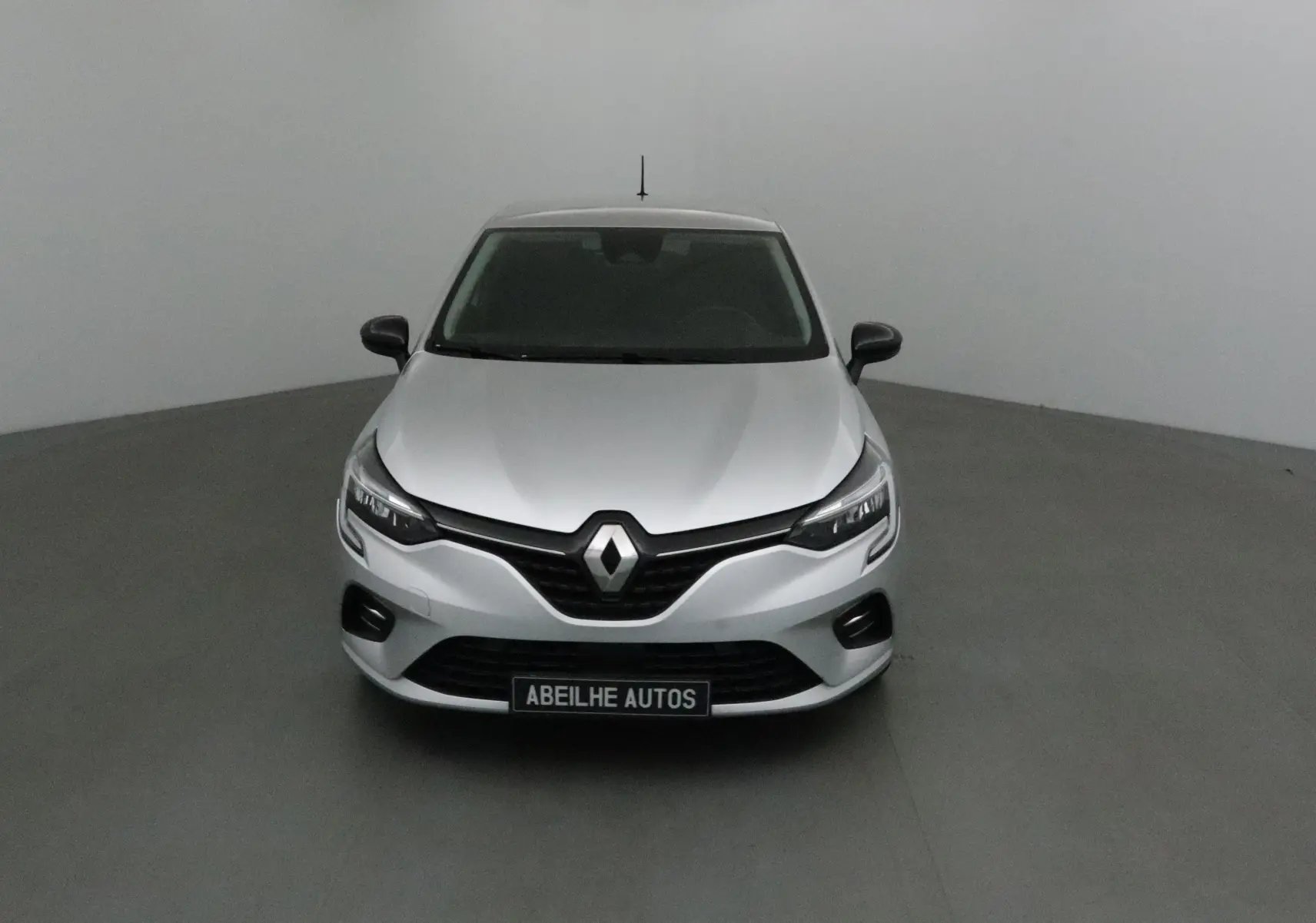 Vue frontale d'une Renault Clio V gris platine 2021 avec calandre noire et phares LED allumés.