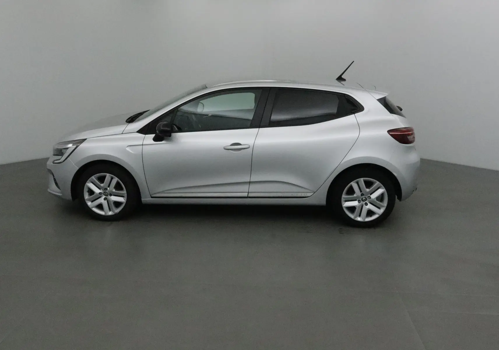 Profil côté gauche d'une Renault Clio V gris platine, compacte et moderne, dans un intérieur neutre et épuré.