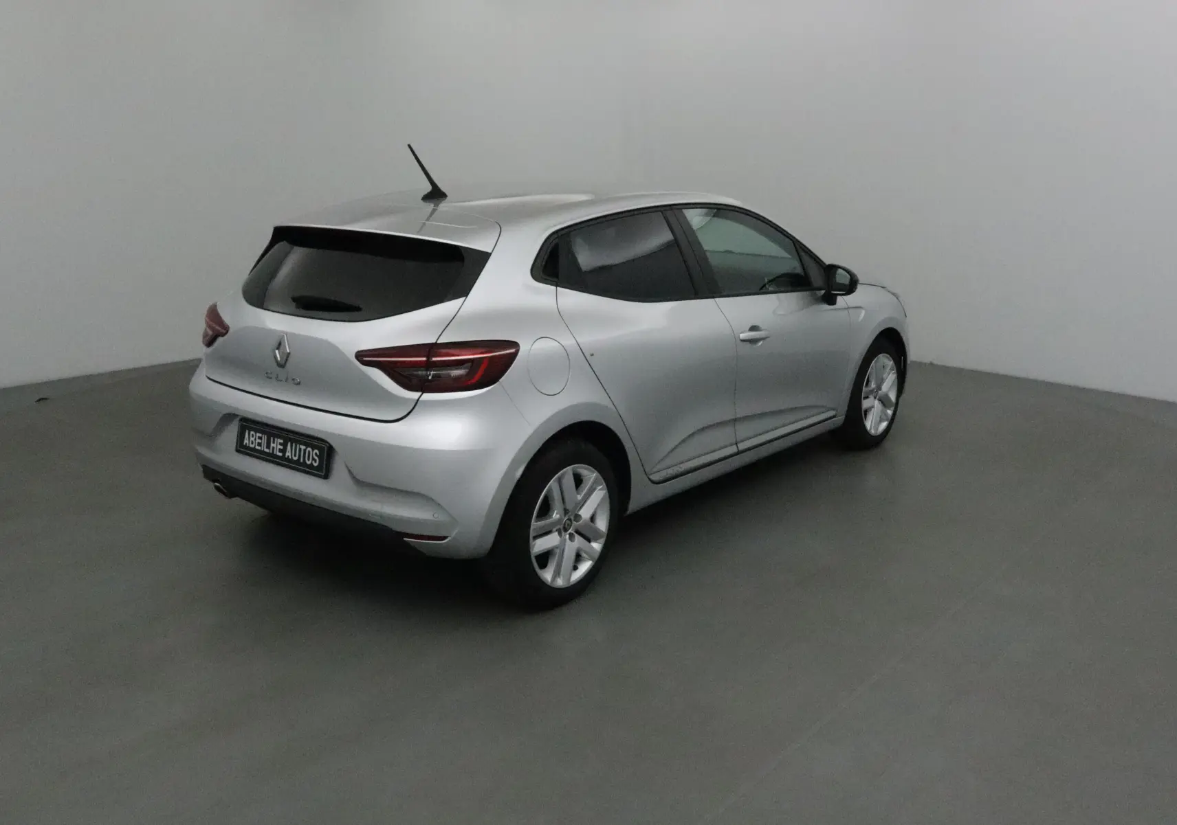 Renault Clio V gris platine vue 3/4 arrière droit dans un studio, avec vitres teintées et jantes alliage.