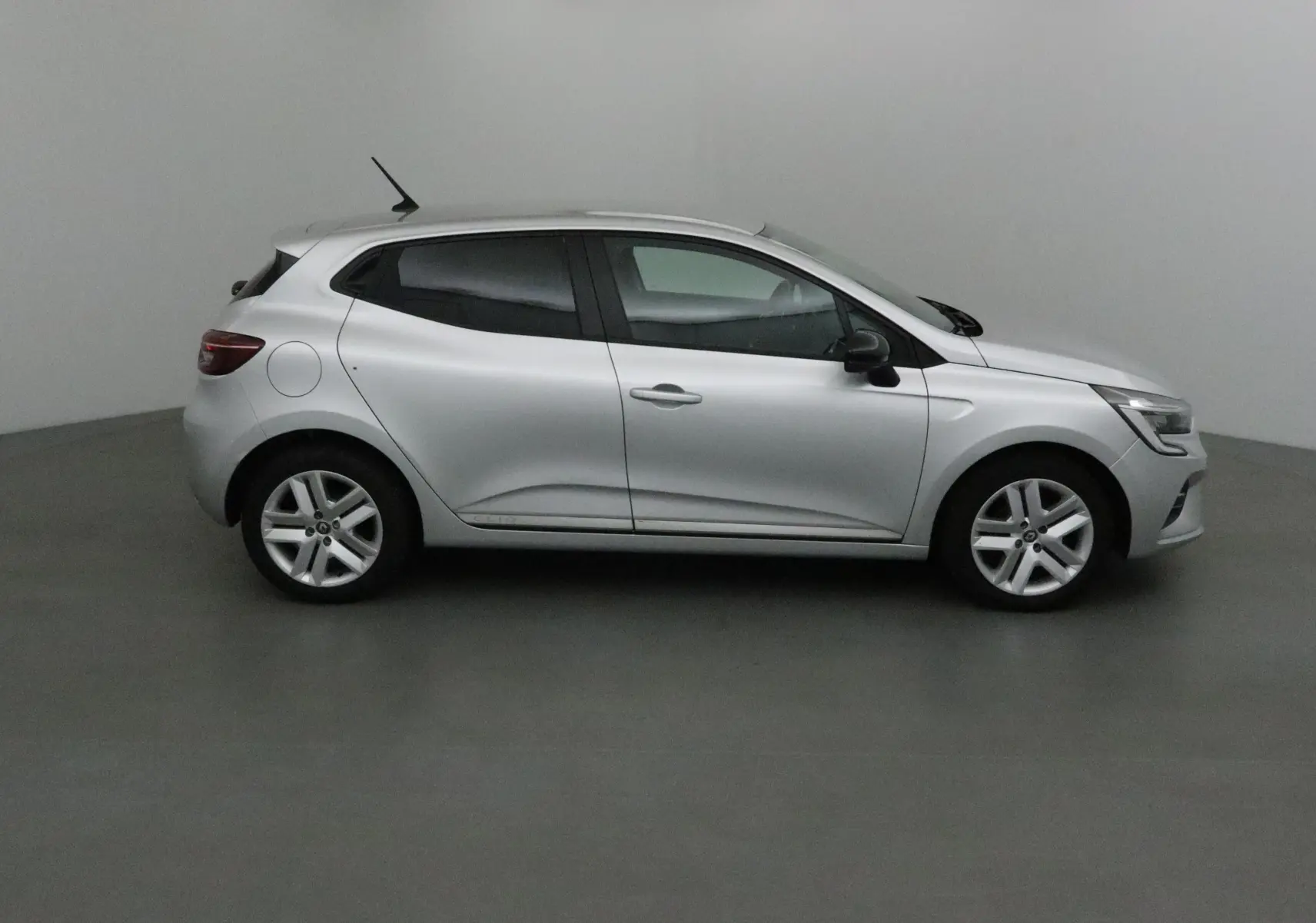 Profil côté droit d'une Renault Clio V gris platine 2021, compacte et moderne, sur fond neutre intérieur.
