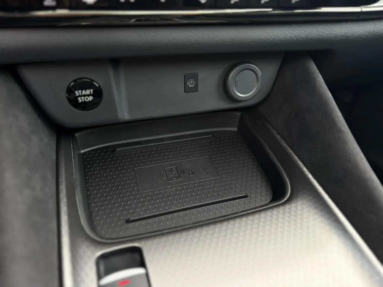 Gros plan sur la console centrale du Nissan Qashqai gris Ceramic, mettant en valeur le chargeur à induction et le bouton Start/Stop.