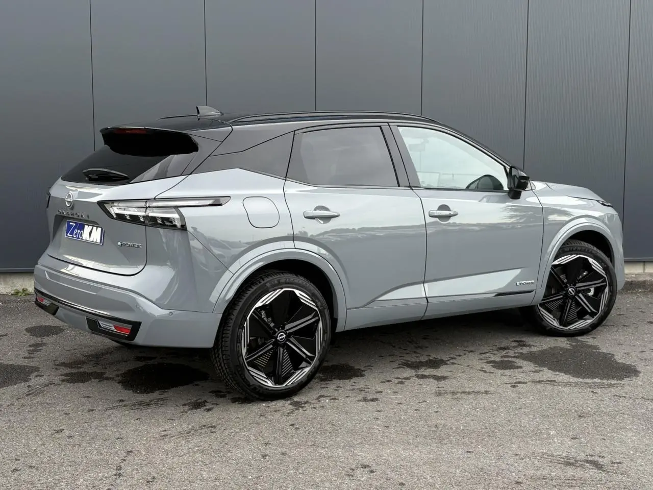 Nissan Qashqai gris Ceramic en 3/4 arrière droit, toit noir panoramique et jantes alliage noires distinctives.