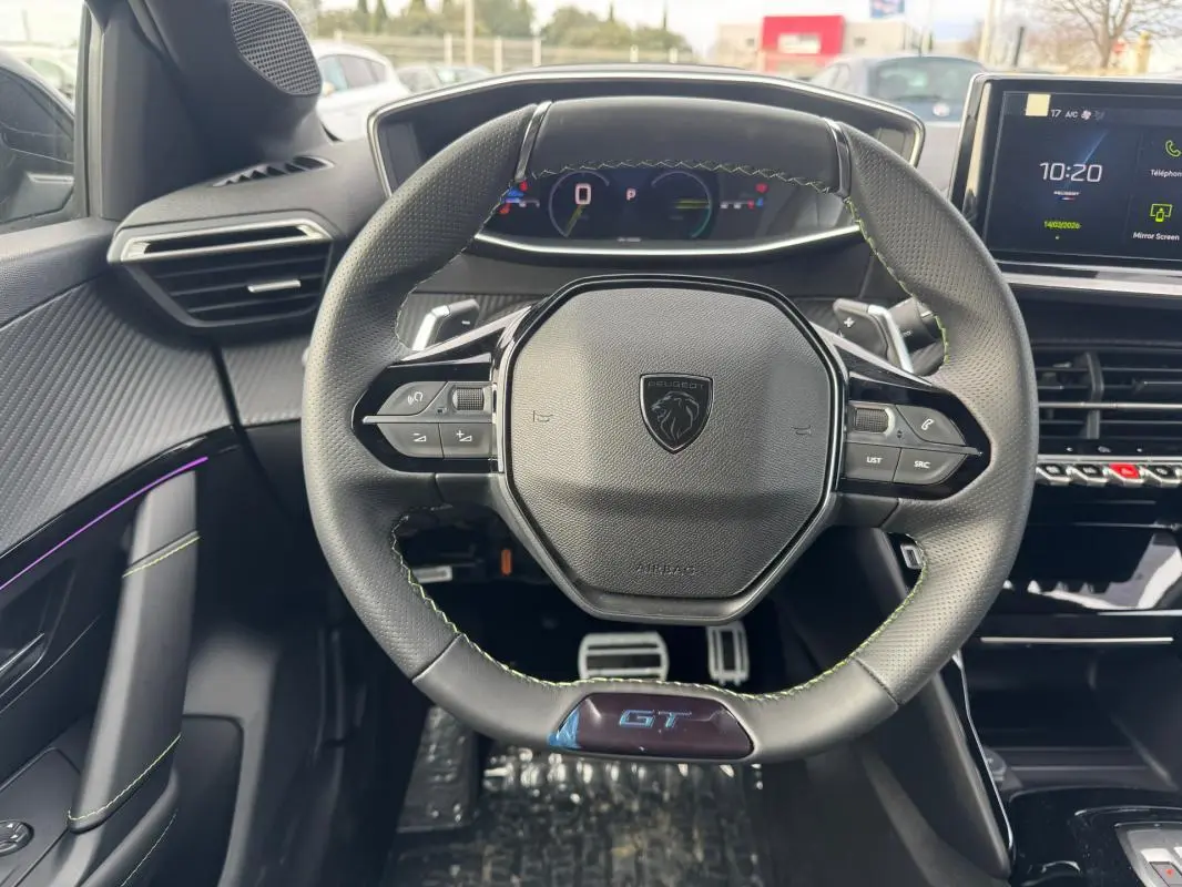 Vue intérieure centrée sur le volant GT noir avec surpiqûres vertes et tableau de bord numérique de la Peugeot 208 Hybrid 2025.