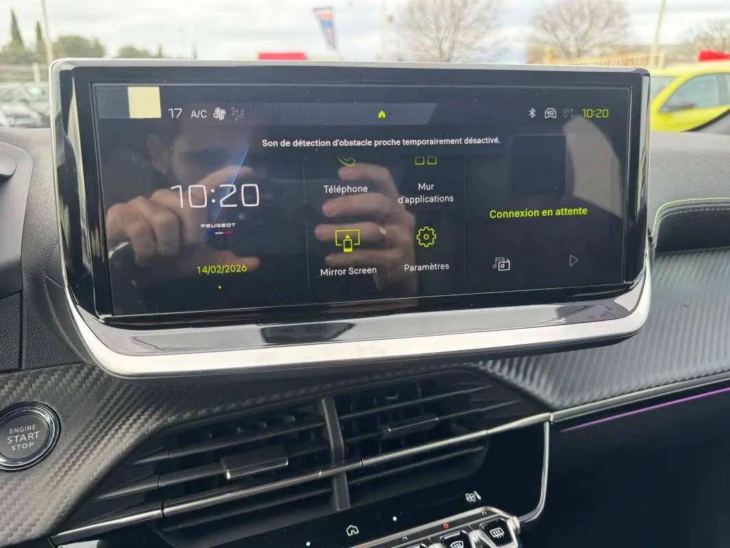 Écran tactile central allumé du tableau de bord de la Peugeot 208 Hybrid 110 gris, avec commandes visibles et finition carbone.