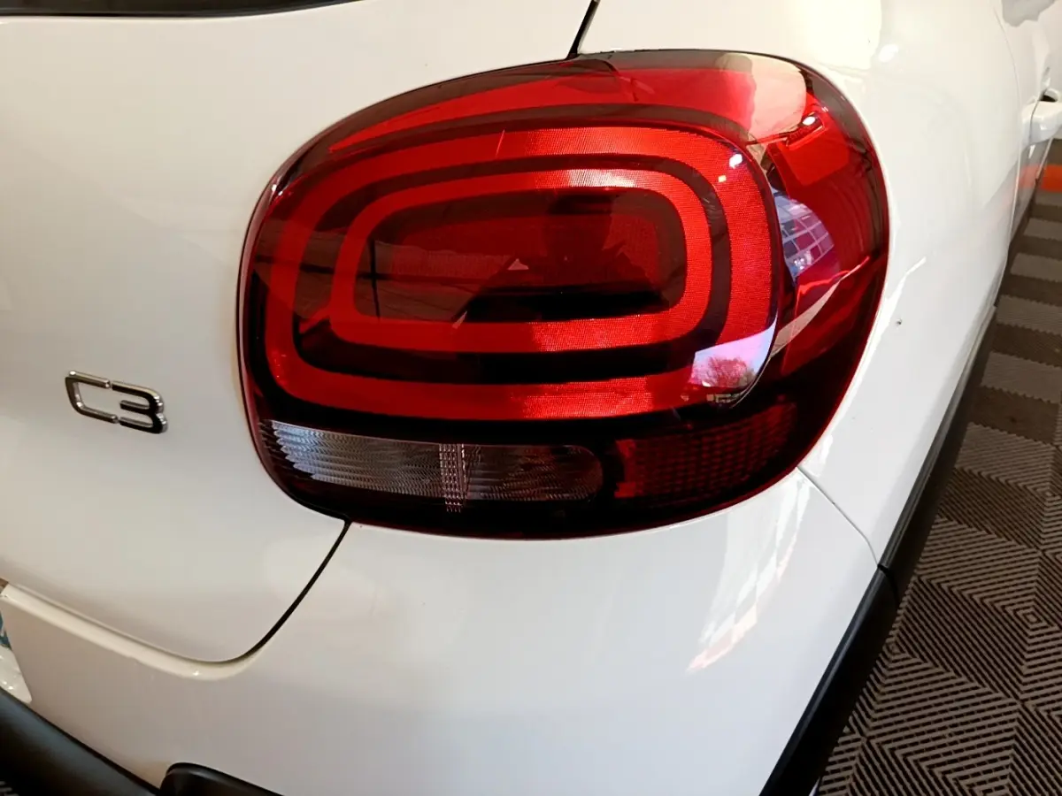 Gros plan sur le feu arrière droit rouge d'une Citroën C3 blanche, avec logo C3 visible sur la carrosserie.