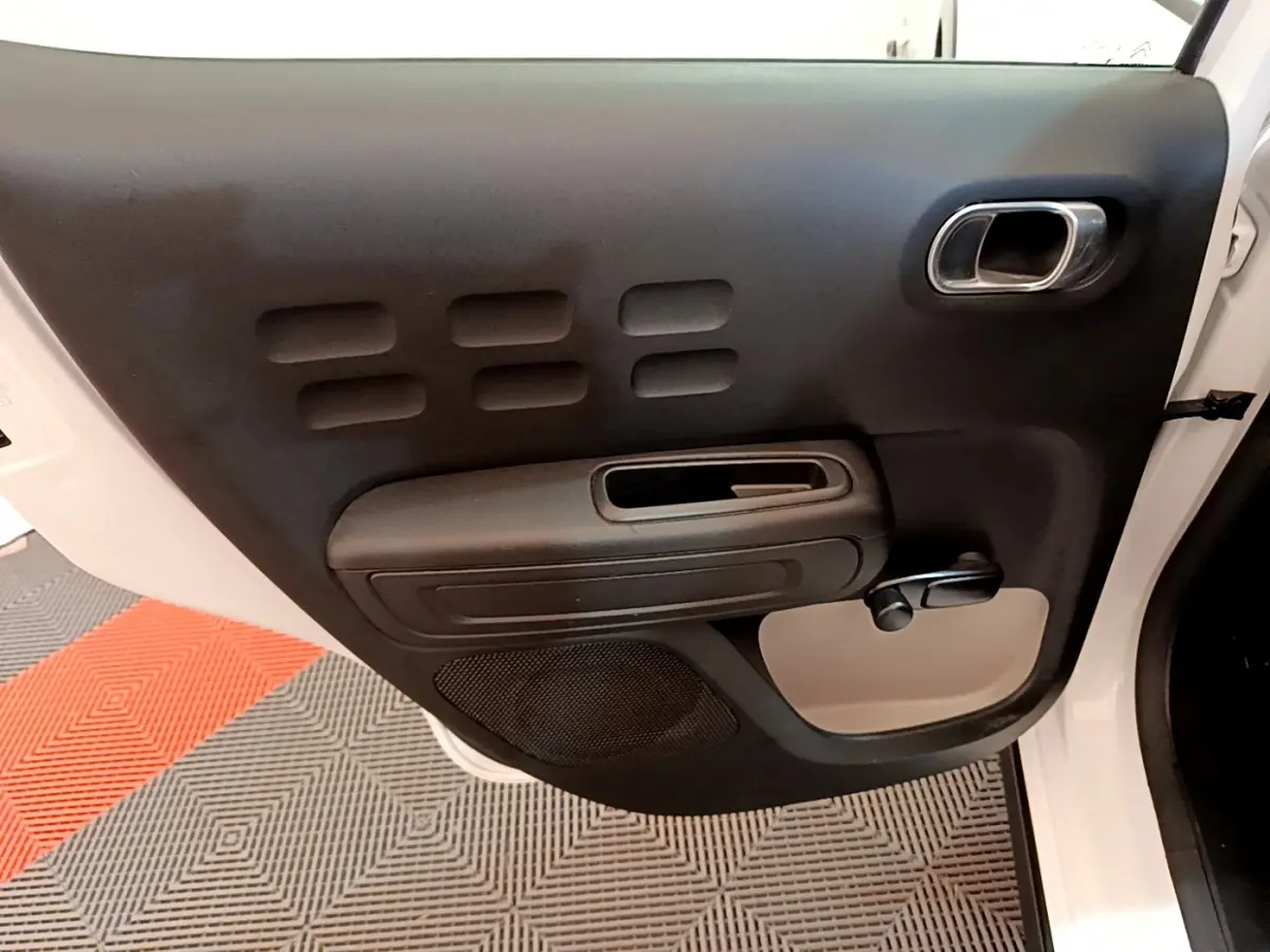 Vue rapprochée de la porte arrière gauche noire et blanche d’une Citroën C3 2022 avec poignée intégrée et manivelle de vitre.
